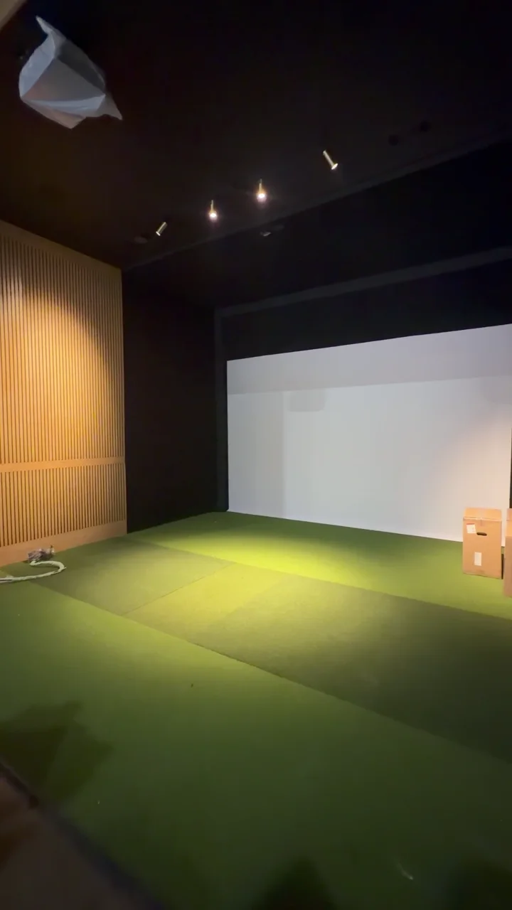 A simulator bay during fit-out, with green turf, screen and timber partitions
